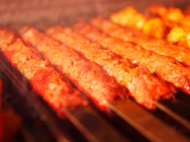Nahaufnahme von traditionellen türkischen Adana Kebap Spießen, die frisch auf einem Holzkohlegrill zubereitet werden.